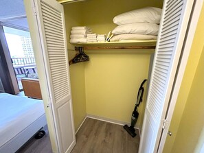 Habitació petita amb un llit, un armari amb prestatges i un aspirador.