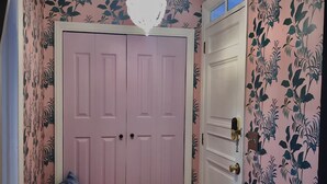 Un pasillo con una puerta rosa, un banco y papel tapiz floral.
