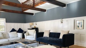 Una sala de estar con un sofá azul oscuro, un sillón blanco y un otoman beige. En el centro, hay una mesa de centro de vidrio.