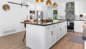 A modern kitchen with white cabinetry, a central island, pendant lighting, and a stainless steel refrigerator. - Paradise Cove with Mountain-Views Pool & Spa  (La Quinta)