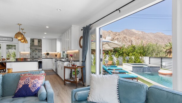 A modern living room with a pool view, a kitchen, and a dining area. - Paradise Cove with Mountain-Views Pool & Spa  (La Quinta)