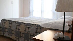 Ein Schlafzimmer mit einem Bett, einem Nachttisch, einer Lampe und einem Fenster mit Vorhängen.