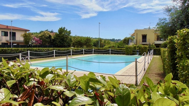 Ein von Grün umgebener Swimmingpool mit Zaun und Gebäuden im Hintergrund.