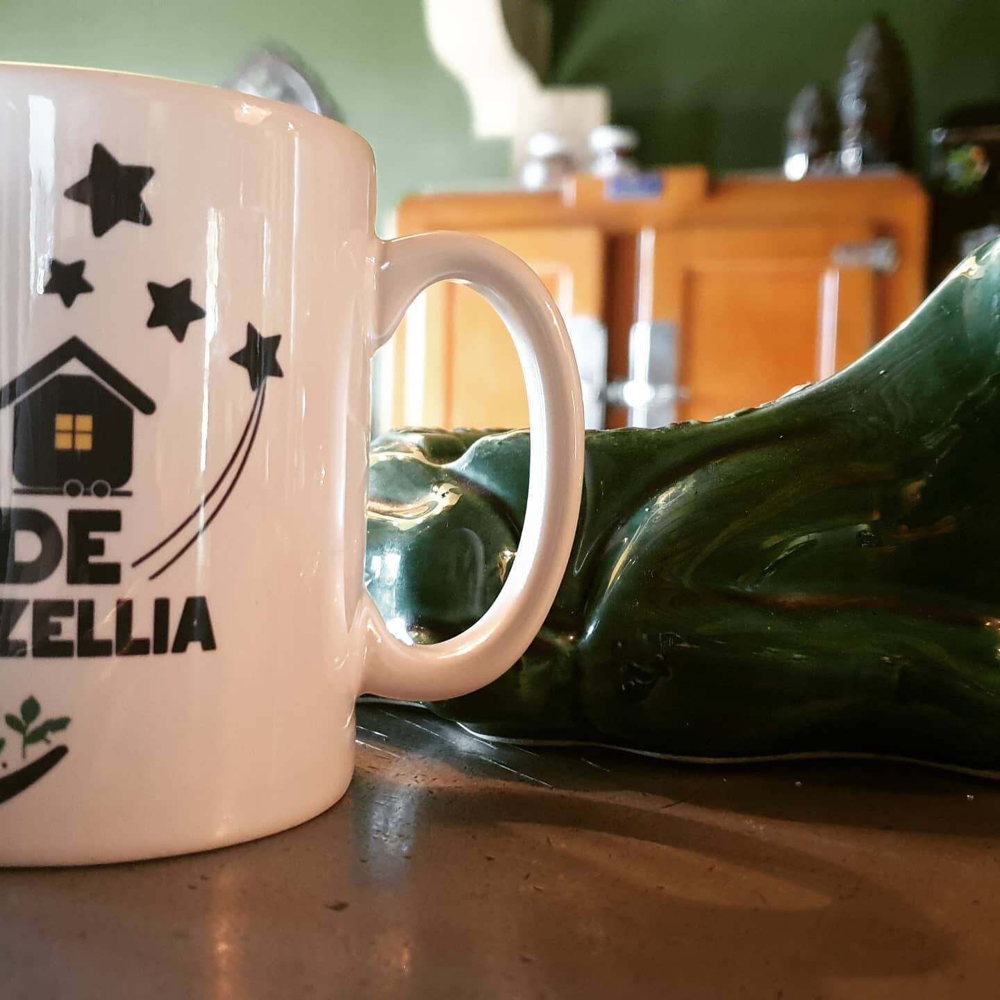 Une tasse blanche ornée d’un motif représentant une maison, des étoiles et le texte « DE ZELLIA ».