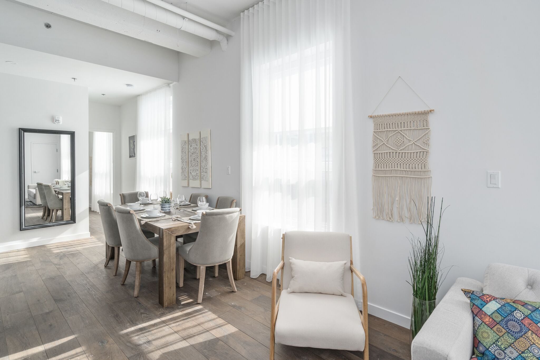 Uma zona de refeições moderna com uma mesa e cadeiras de madeira, uma cadeira branca e um painel de parede em macramé.