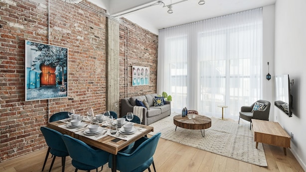 A modern living room with a brick wall, a dining area with blue chairs, and a sofa with a coffee table.