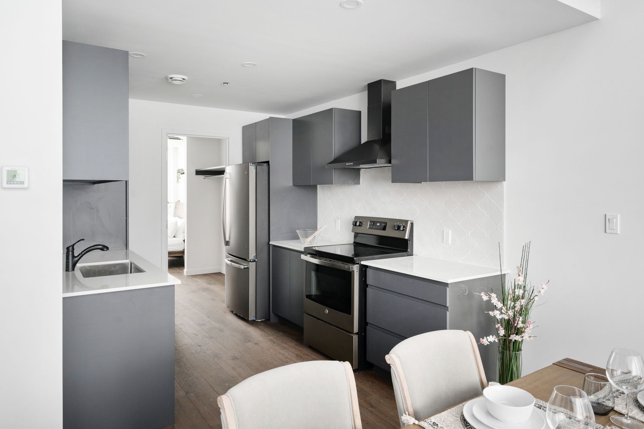 A modern kitchen with grey cabinetry, stainless steel appliances, and a dining area with a table set for two.