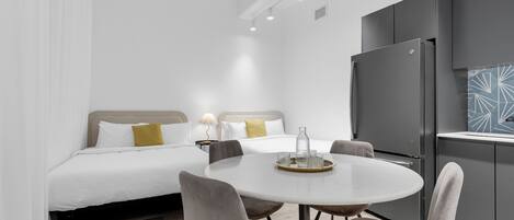 Una habitación de hotel moderna con una cama, una mesa de comedor con sillas, un refrigerador y una pequeña cocina.