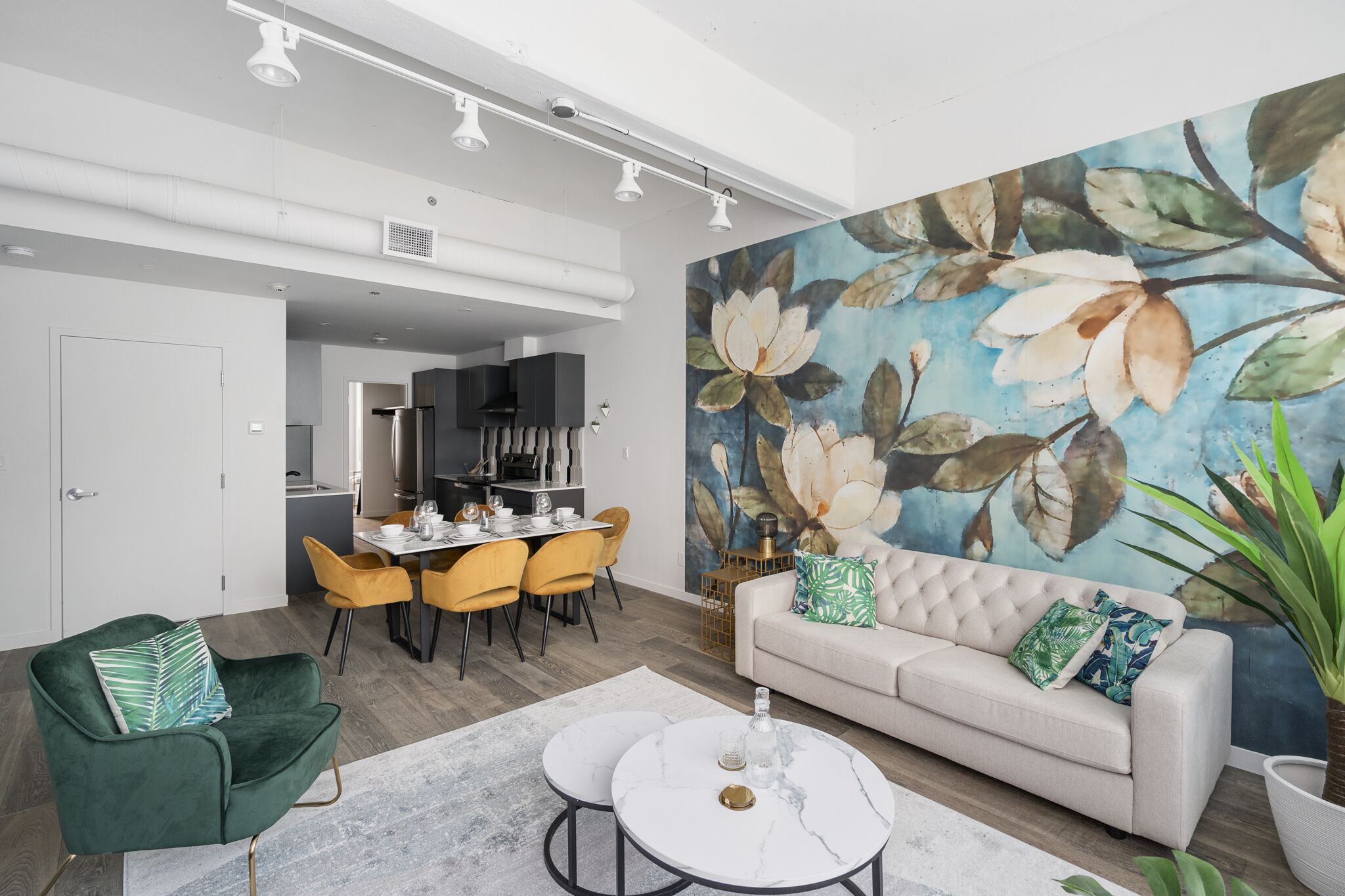 A modern living room with a sofa, two round tables, and a dining area with yellow chairs.