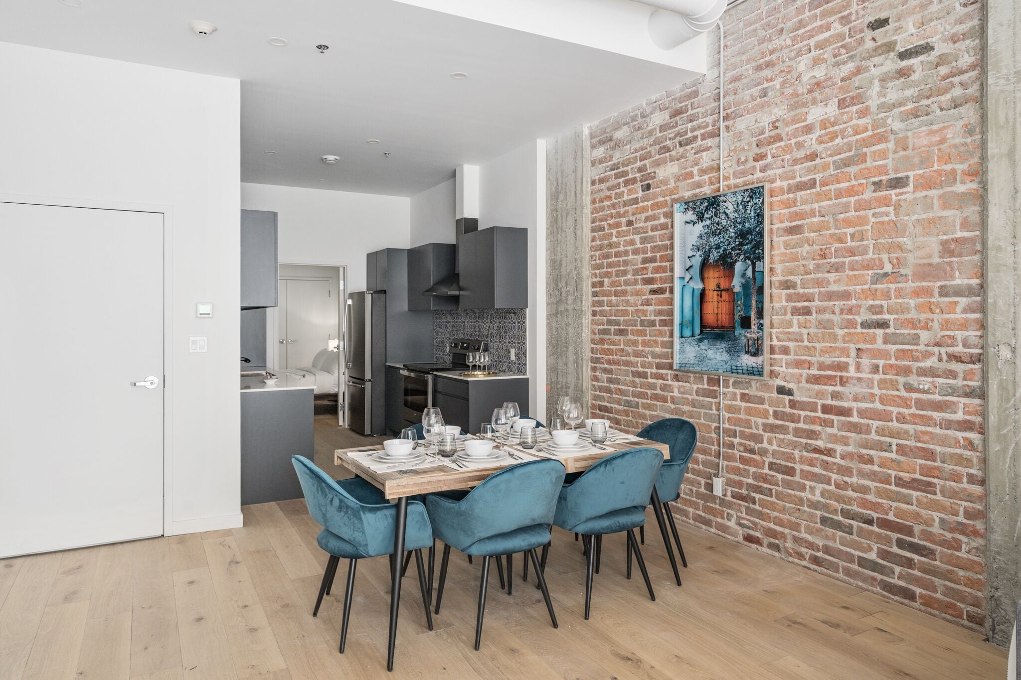 A modern dining area with a brick wall, a wooden table set for four, and a kitchen in the background.