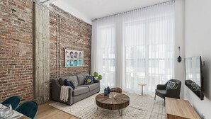 A modern living room with a brick wall, a grey sofa, a round coffee table, and a TV mounted on the wall.
