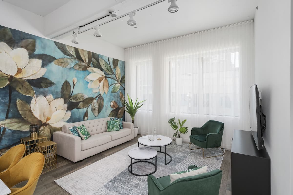A modern living room with a large floral mural, a sofa, two round coffee tables, a green armchair, and a flat-screen TV.
