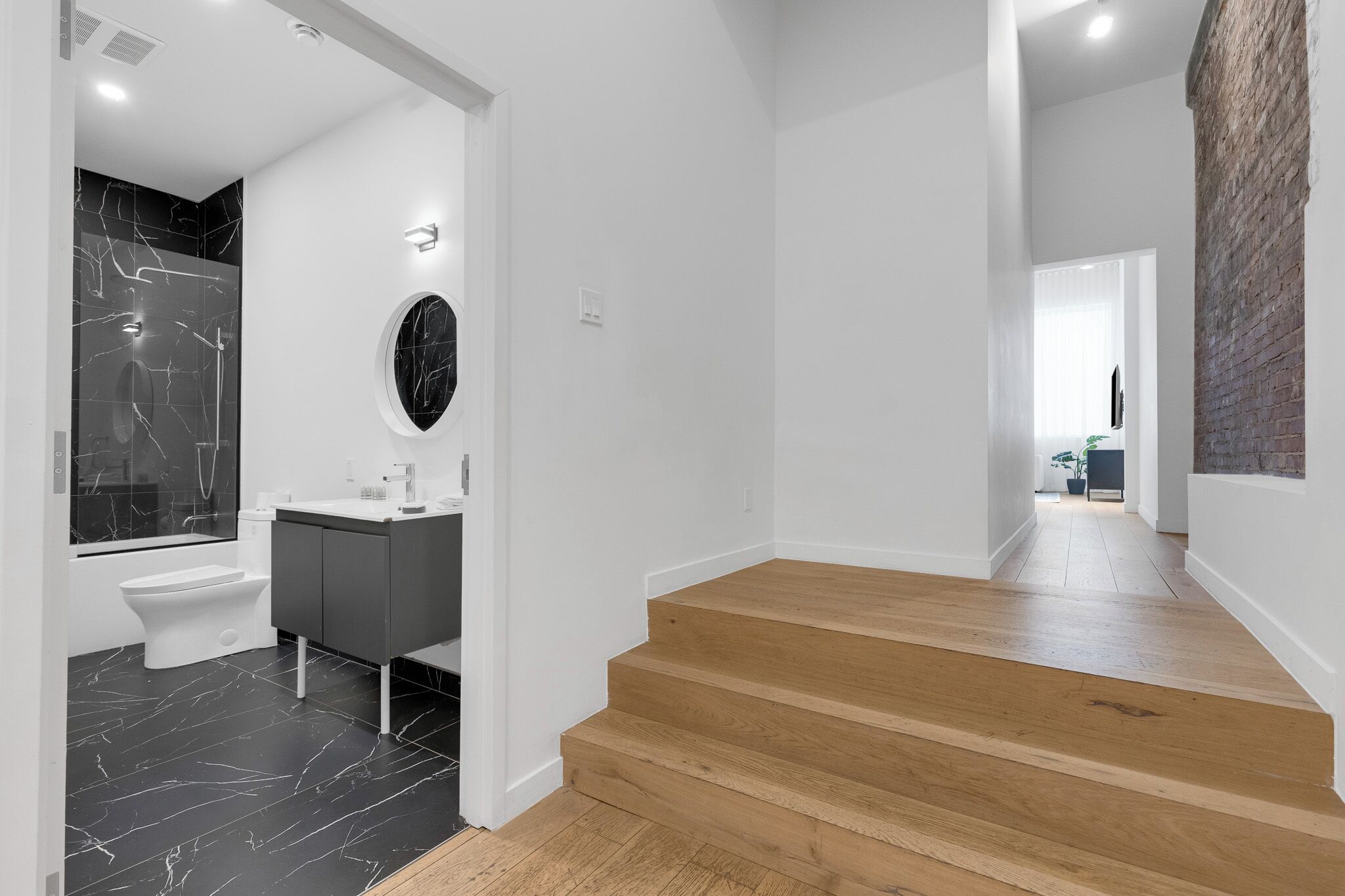 A modern bathroom with a black marble sink, a toilet, and a shower. There is a wooden staircase leading to another room.