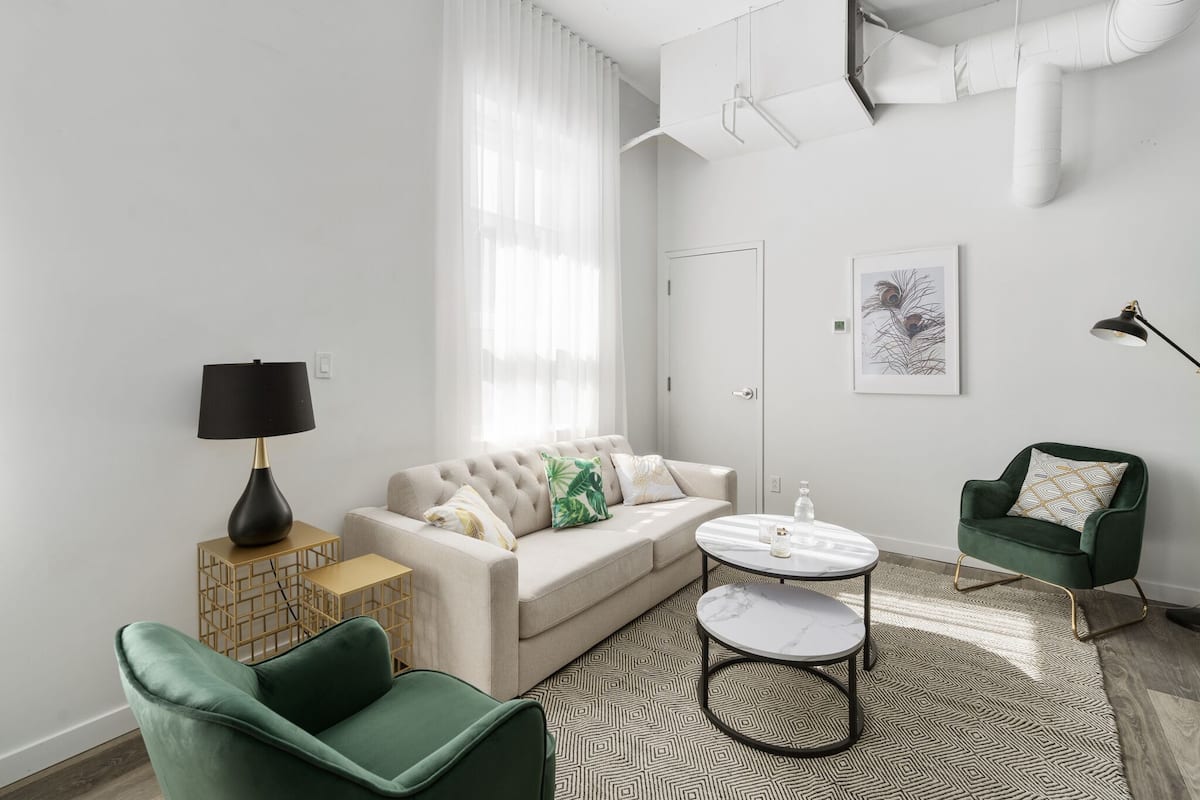 A modern living room with a beige sofa, green armchairs, a round coffee table, and a floor lamp.