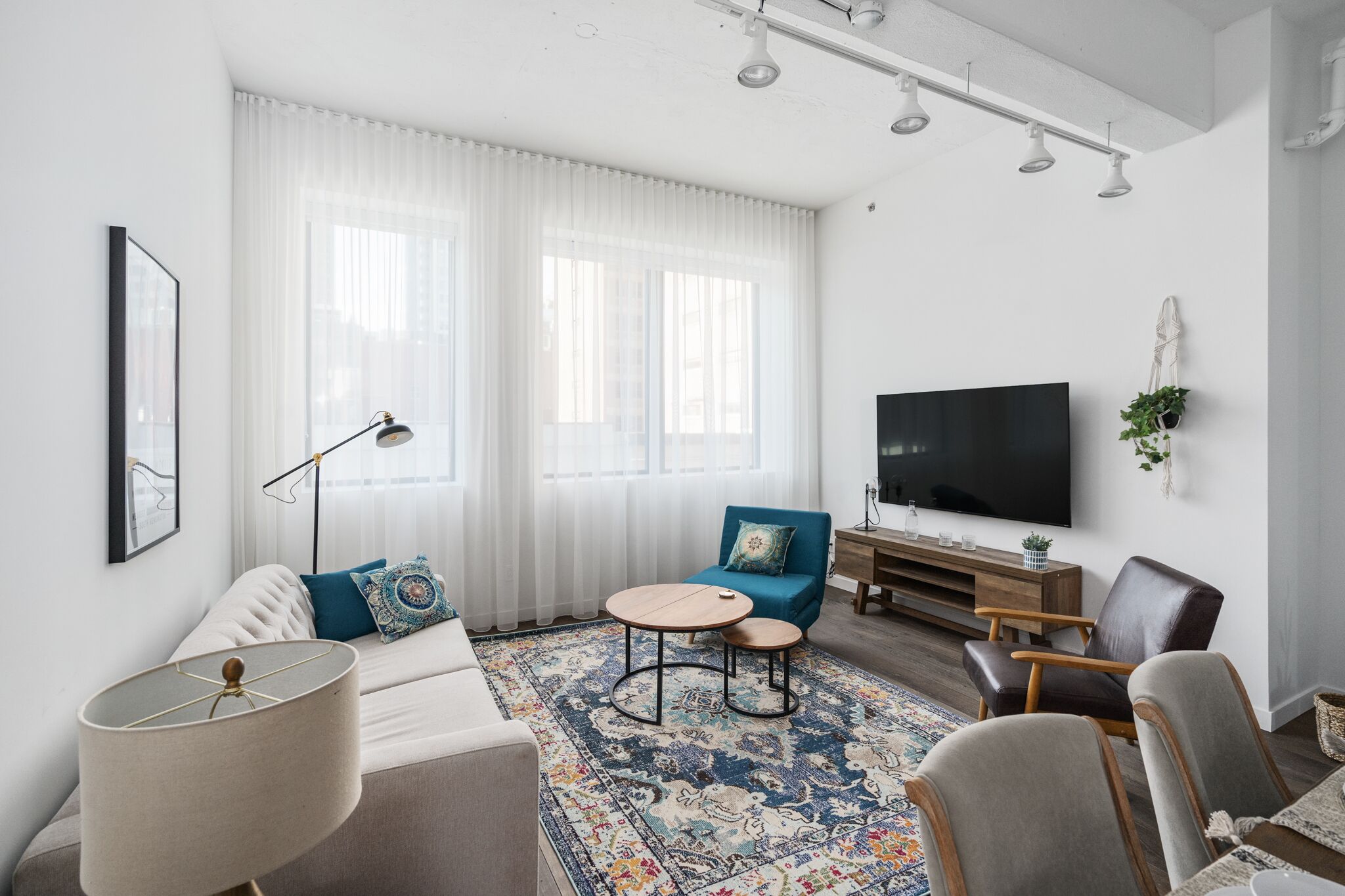Un salon moderne avec un canapé, une table basse, un téléviseur et une grande fenêtre ornée de rideaux légers.