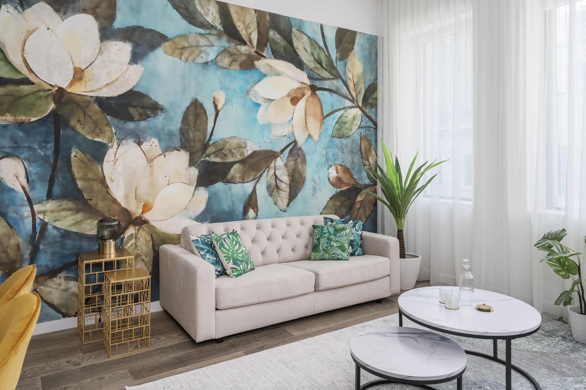 A living room with a large floral mural, a beige sofa, a round coffee table, and a potted plant.