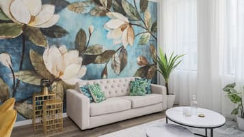 A living room with a large floral mural, a beige sofa, a round coffee table, and a potted plant.