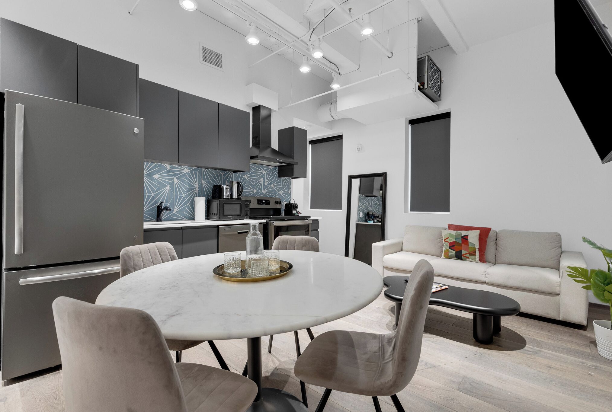 Een moderne keuken met een inbouwoven, een eethoek met een ronde tafel en stoelen, en een zithoek met een bank en salontafel.