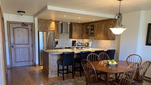 A modern kitchen with wooden cabinets, a stainless steel refrigerator, and a dining area with a table set for four. - Beaver Creek Ski-in/Ski-out Condo (Avon)