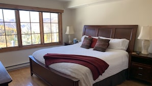 A bedroom with a large bed, wooden headboard, two bedside tables with lamps, and a window with a view of mountains. - Beaver Creek Ski-in/Ski-out Condo (Avon)