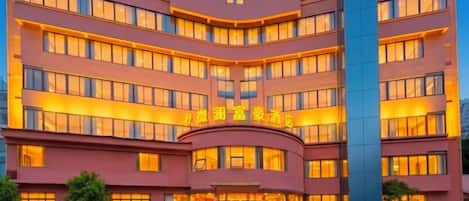 Um hotel com vários andares, fachada curva, janelas iluminadas e entrada central.