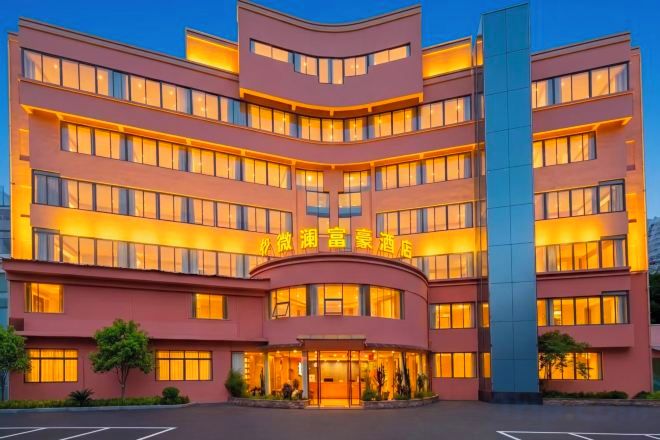 Un hotel de varios pisos con fachada curva, ventanas iluminadas y una entrada central.