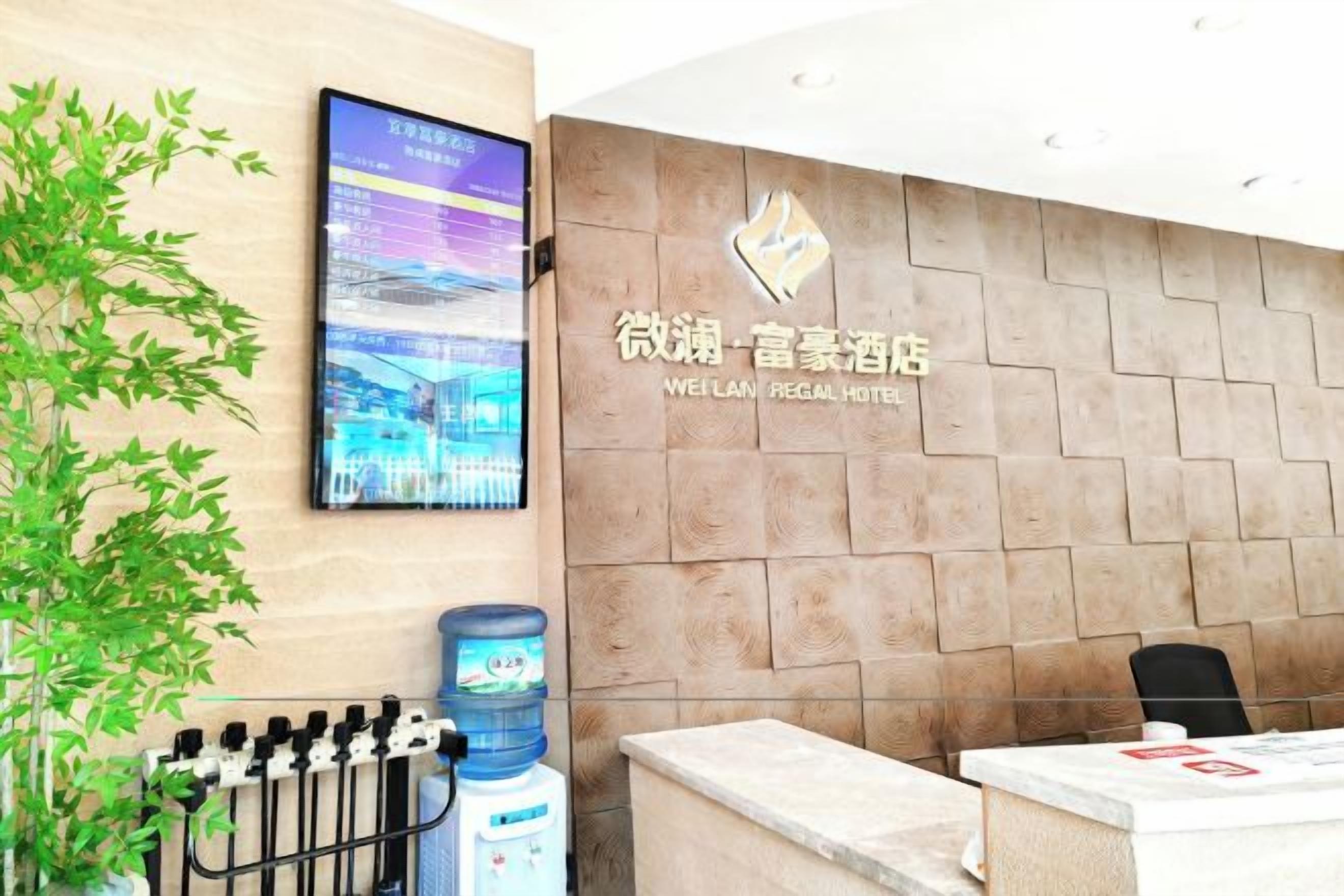 A reception desk with a digital display, a water dispenser, and a sign for the Weilan Regal Hotel.
