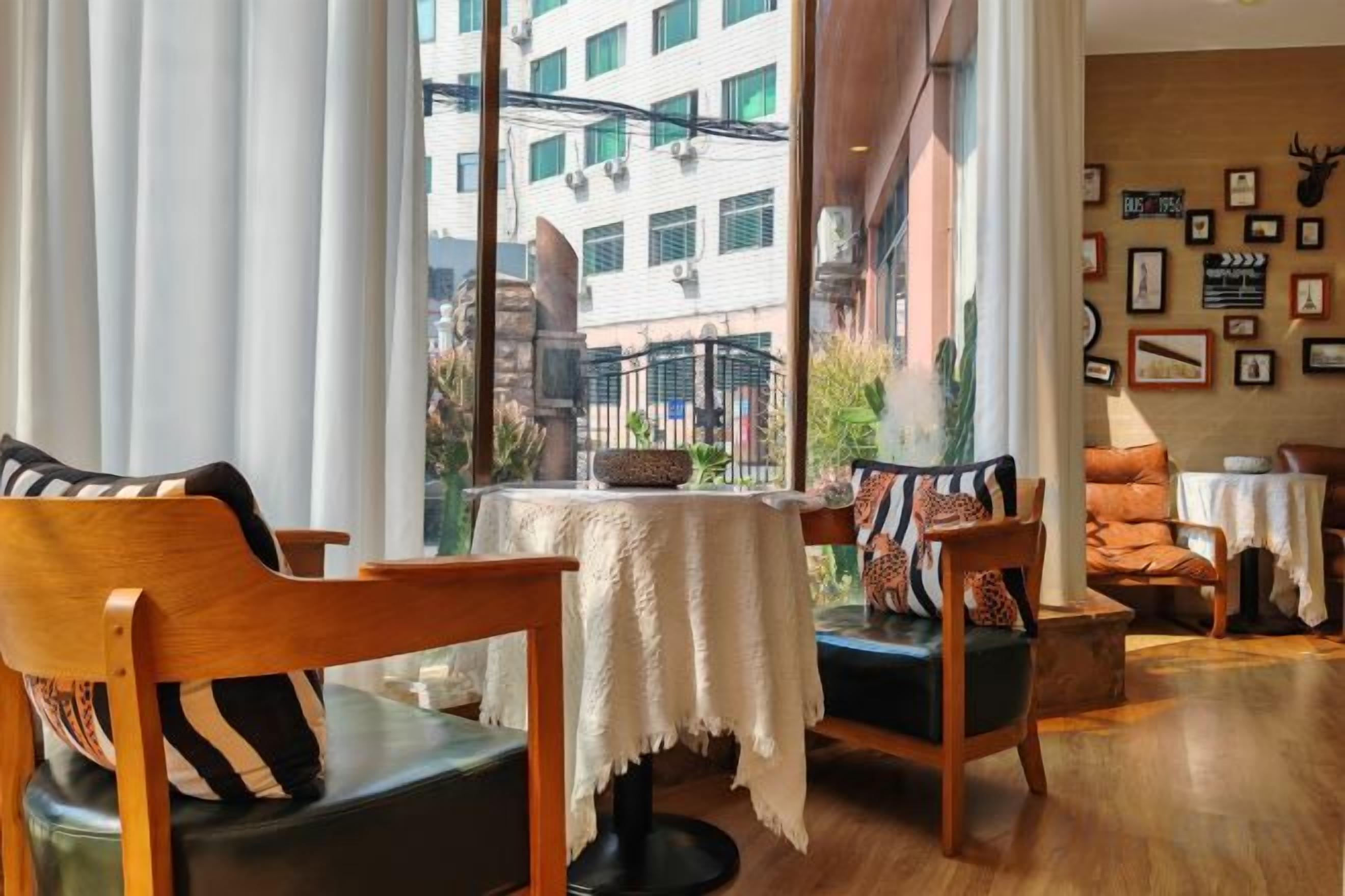 A room with a view of a building, a table with a white tablecloth, and a wall with framed pictures.
