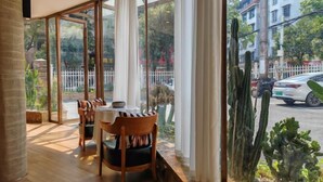 A dining area with a table and chairs, large windows with curtains, and a view of a street with cars and buildings. - Yizhang Fuhao Hotel (Yizhang)