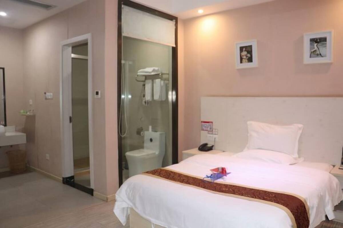 A hotel room with a bed, a bedside table, a nightstand, a bathroom with a shower, a toilet, and a sink.