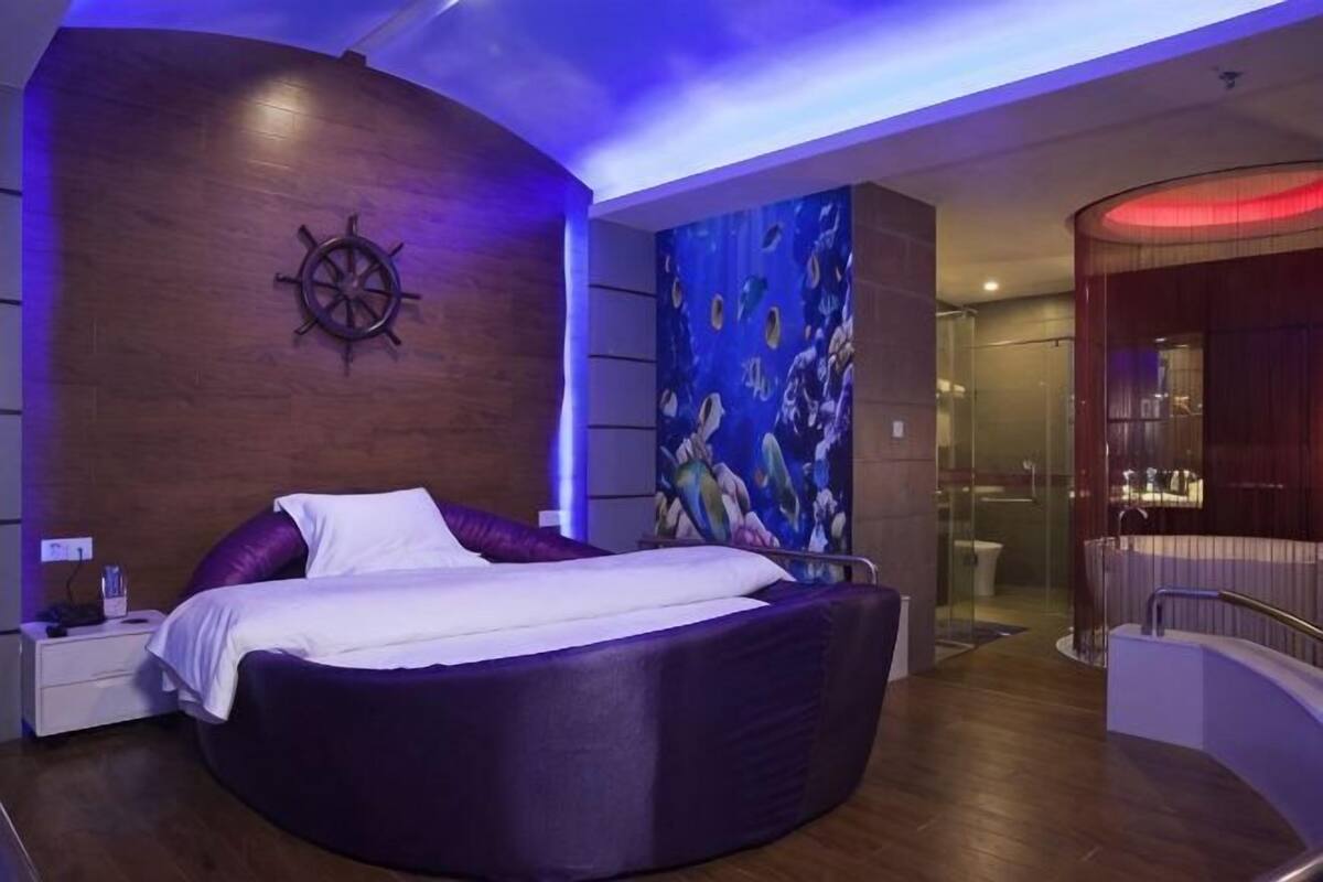 A modern bedroom with a curved bed, a ship's wheel on the wall, and a mural of mermaids.