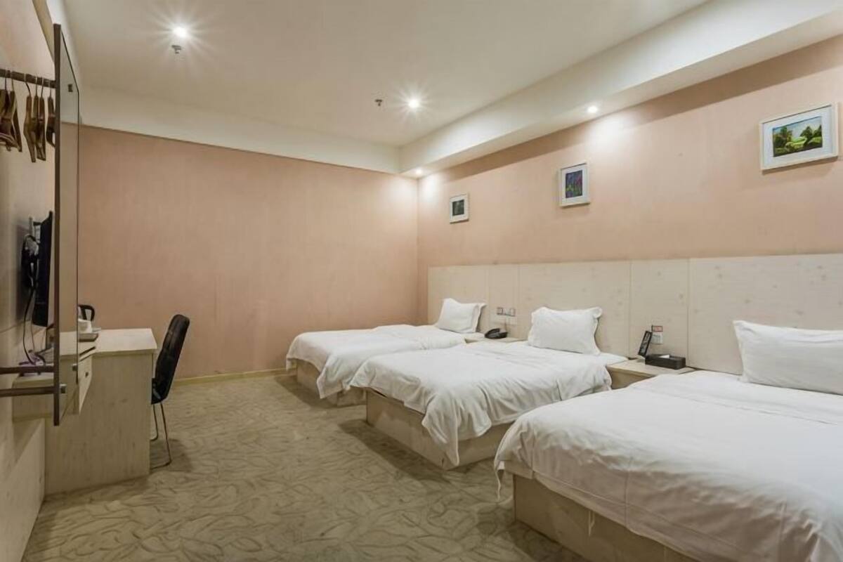 A hotel room with three beds, a desk, a chair, and a small table.