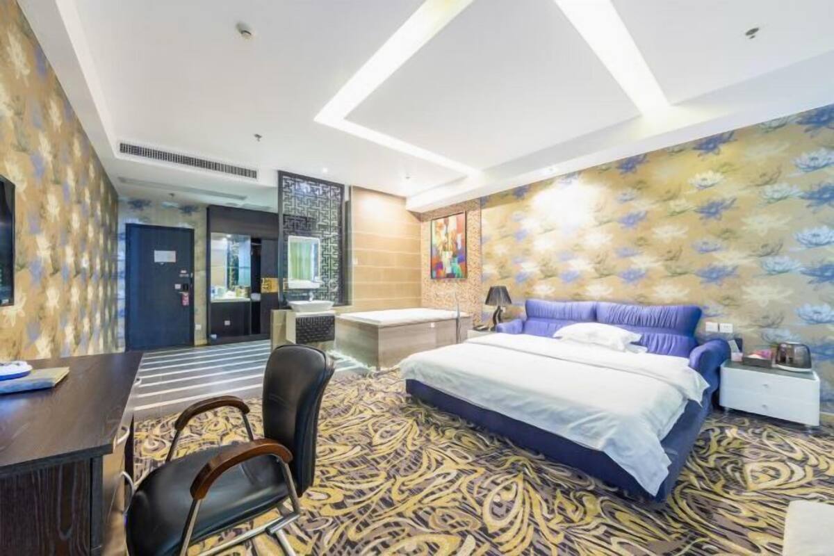 A hotel room with a bed, desk, chair, and a patterned carpet.