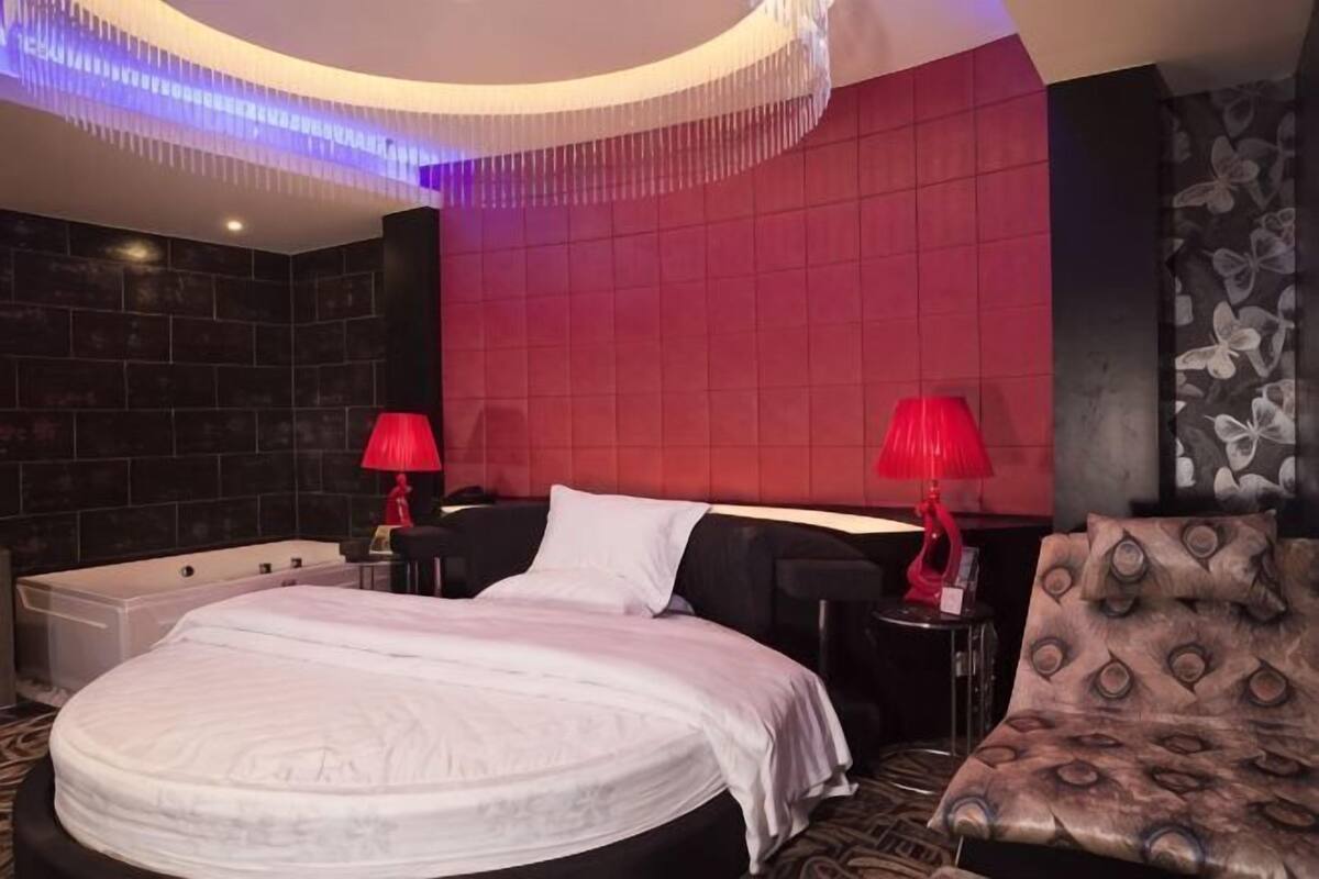 A hotel room with a large bed, two bedside tables, a red lamp, and a patterned sofa.