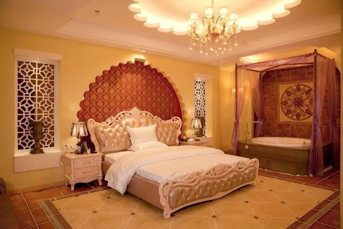 A bedroom with a large bed, a chandelier, a bathtub, and decorative wall panels.