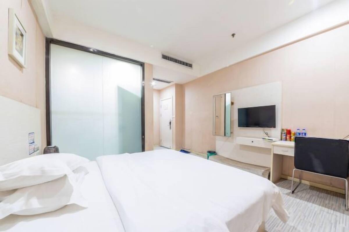 A hotel room with a bed, a desk, a chair, a television, and a sliding door.