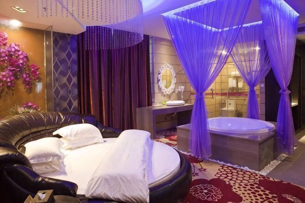 A luxurious bedroom with a large bed, a sitting area, a vanity, and a jacuzzi.