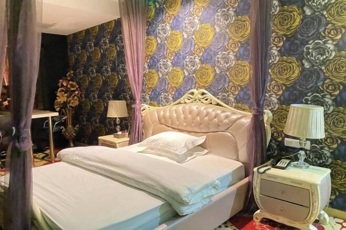 A bed with a headboard, a nightstand with a lamp, and a wall with a floral pattern.