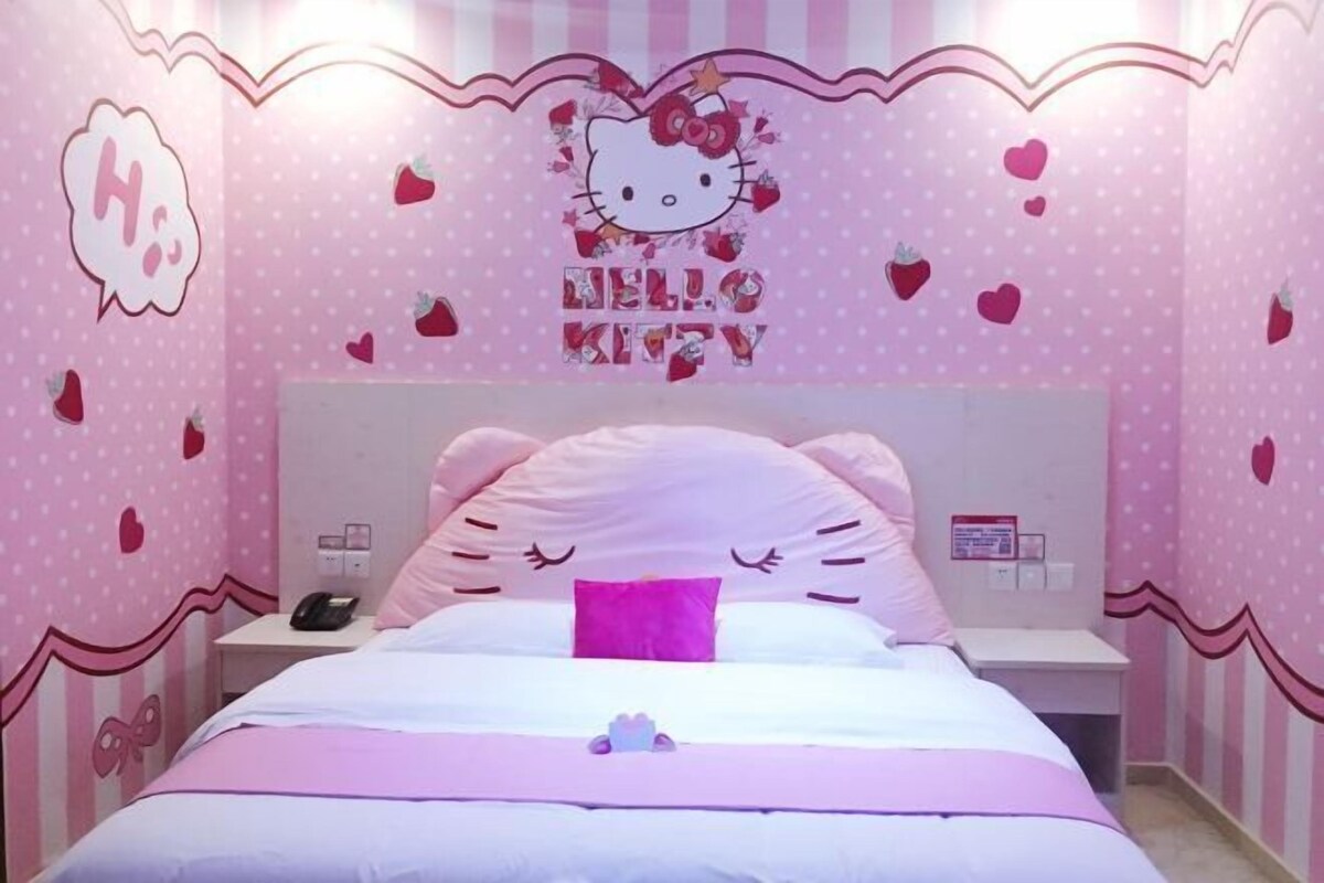 A pink-themed bedroom with a Hello Kitty design, a bed with pink and white bedding, and a nightstand with a phone.