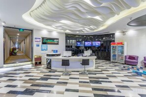 Un vestíbulo de hotel con una recepción, mostrador de registro y una pantalla digital, además de un piso con diseño.