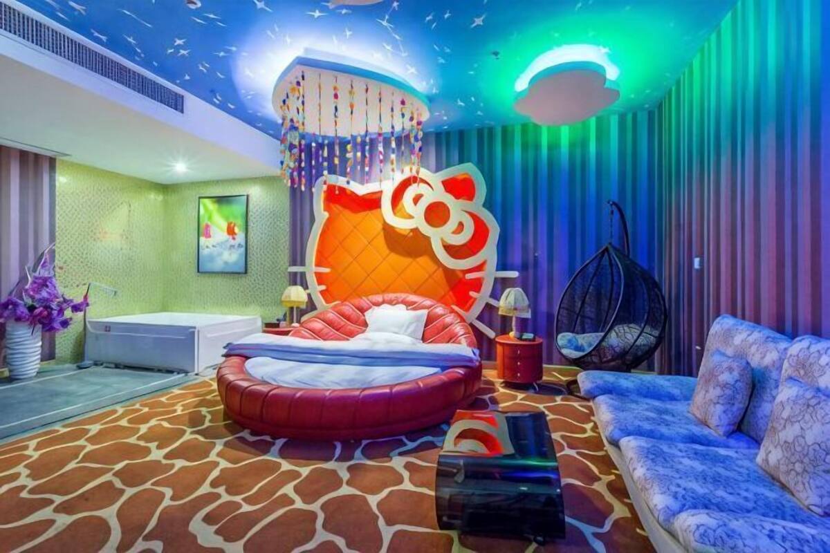 A room with a large, colorful cat-themed headboard, a round bed, a sofa, and a hanging chair.