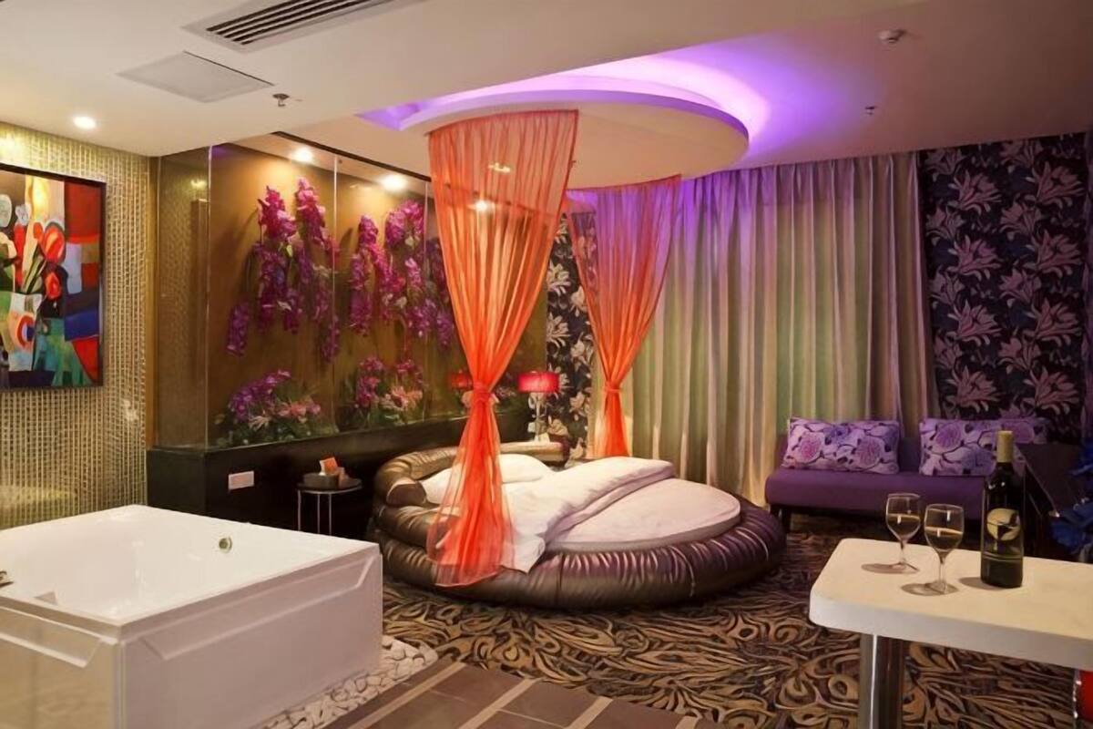 A bedroom with a large bed, a separate sofa, a small table with a bottle and glasses, and a bathtub.