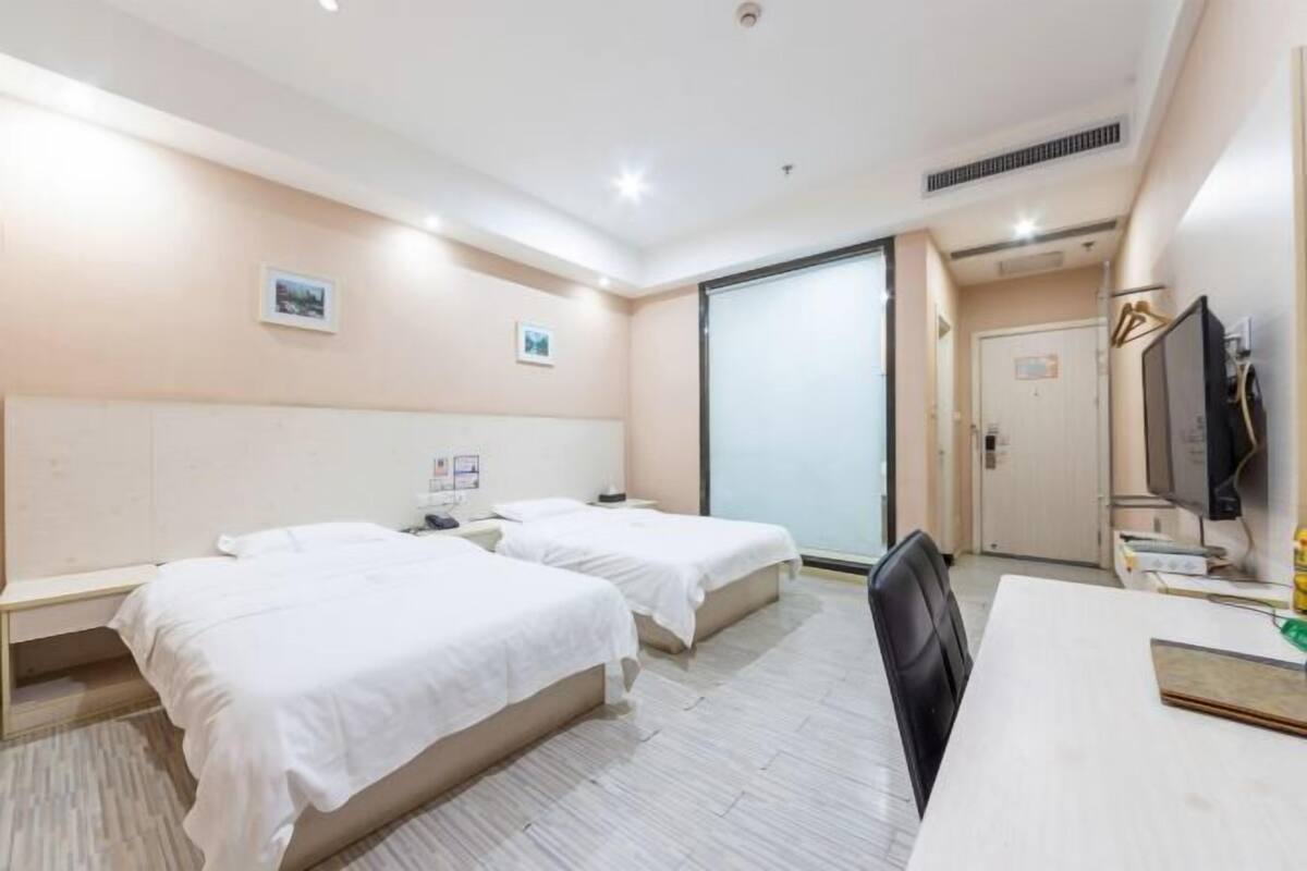A hotel room with two beds, a desk, a chair, a TV, and a sliding door.