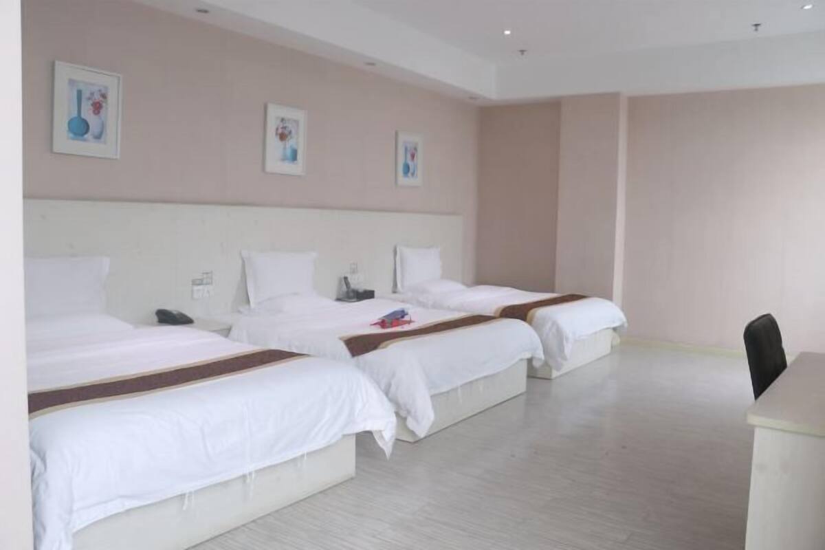 A hotel room with three beds, a desk, and artwork on the walls.