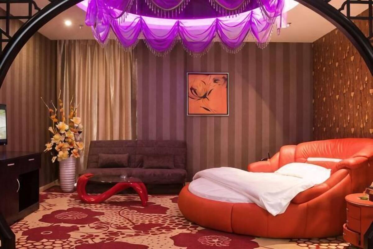 A room with a red massage chair, a dark sofa, a desk, and a vase of flowers.