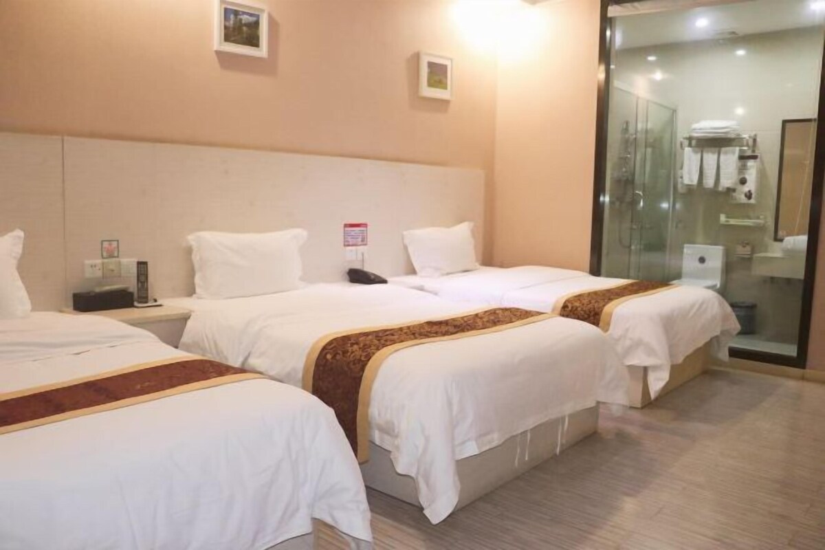 A hotel room with three beds, a bedside table with a phone, a small picture on the wall, and a glass shower enclosure.