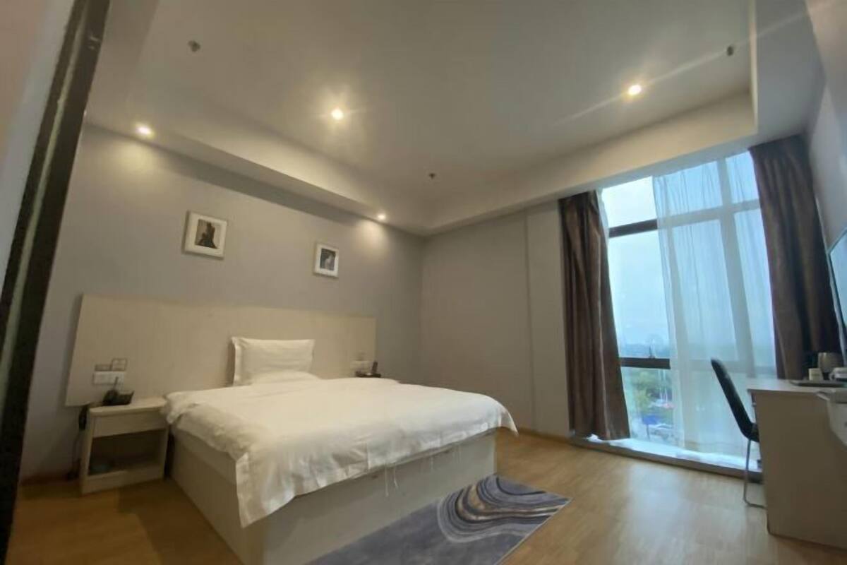 A bedroom with a bed, bedside tables, a desk, and a large window.