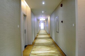 Un pasillo de hotel con pisos alfombrados, puertas a ambos lados y una fuente de luz al final.