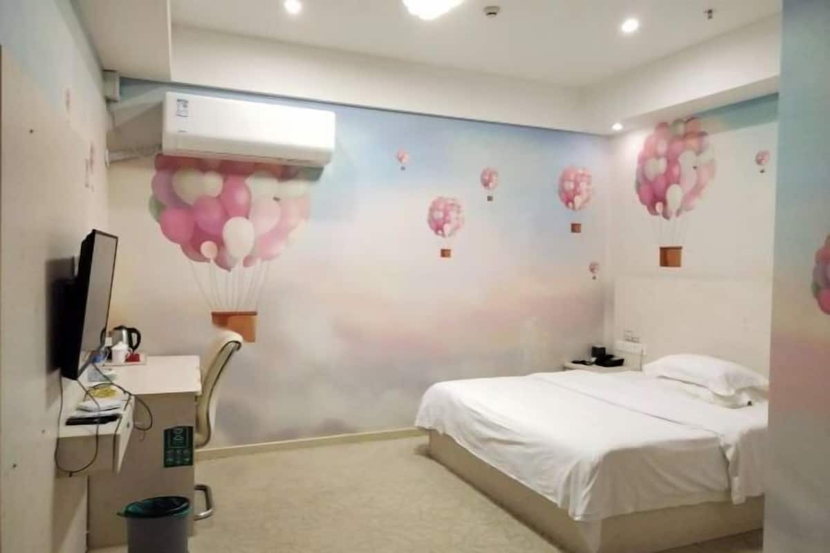 A bedroom with a bed, a desk with a chair, an air conditioner, and a wall with balloon decorations.