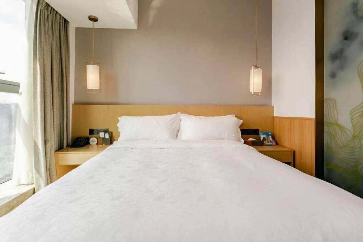 A hotel room with a large bed, wooden headboard, bedside tables with lamps, and a window with curtains.